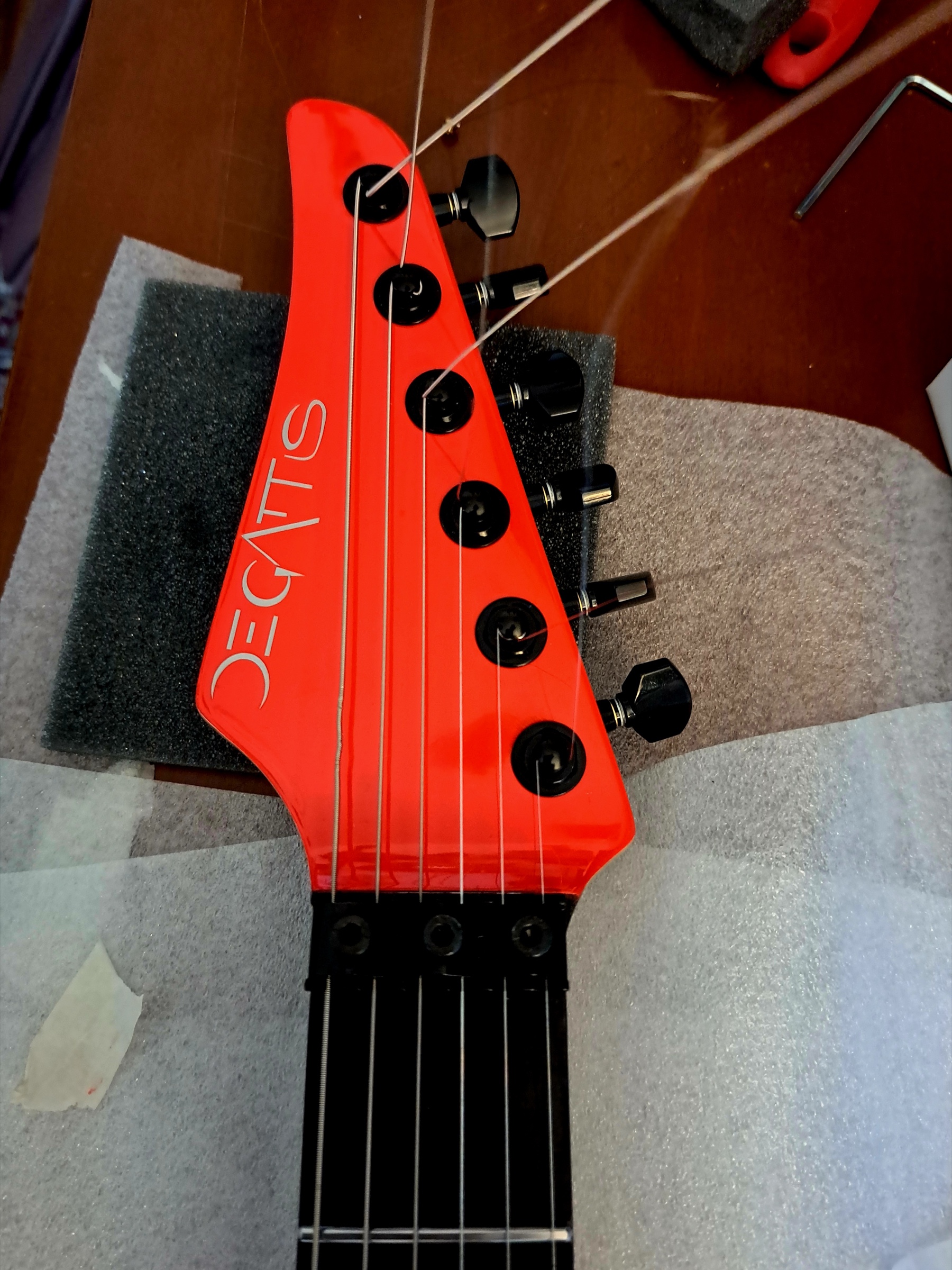 A red headstock with the De Gattis mark, strings and tuners just fitted