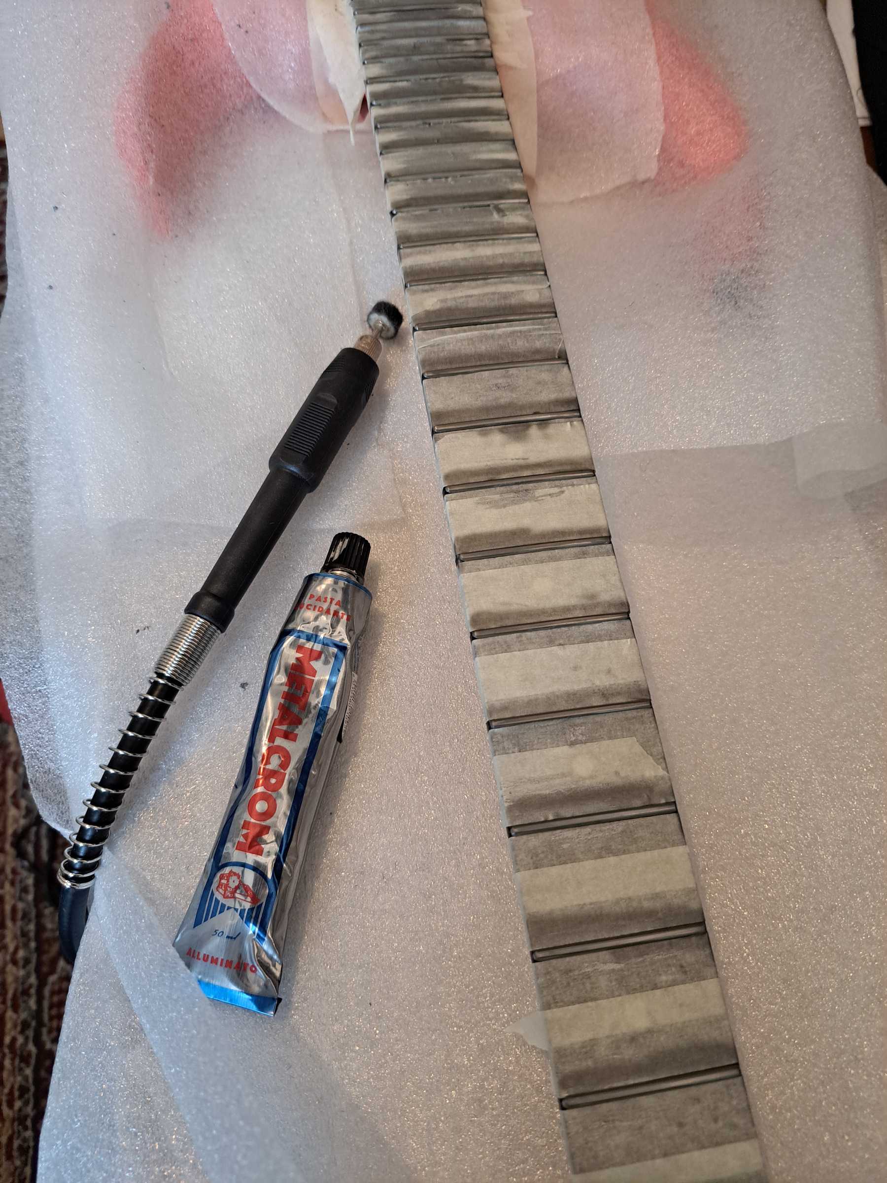 A fingerboard with masked frets, a rotary tool and a tube of polishing paste
