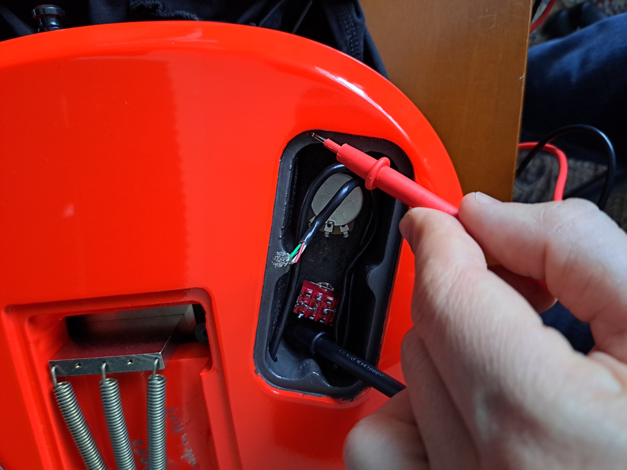 A hand checking the circuit with a tester, inside the cavity of a red body