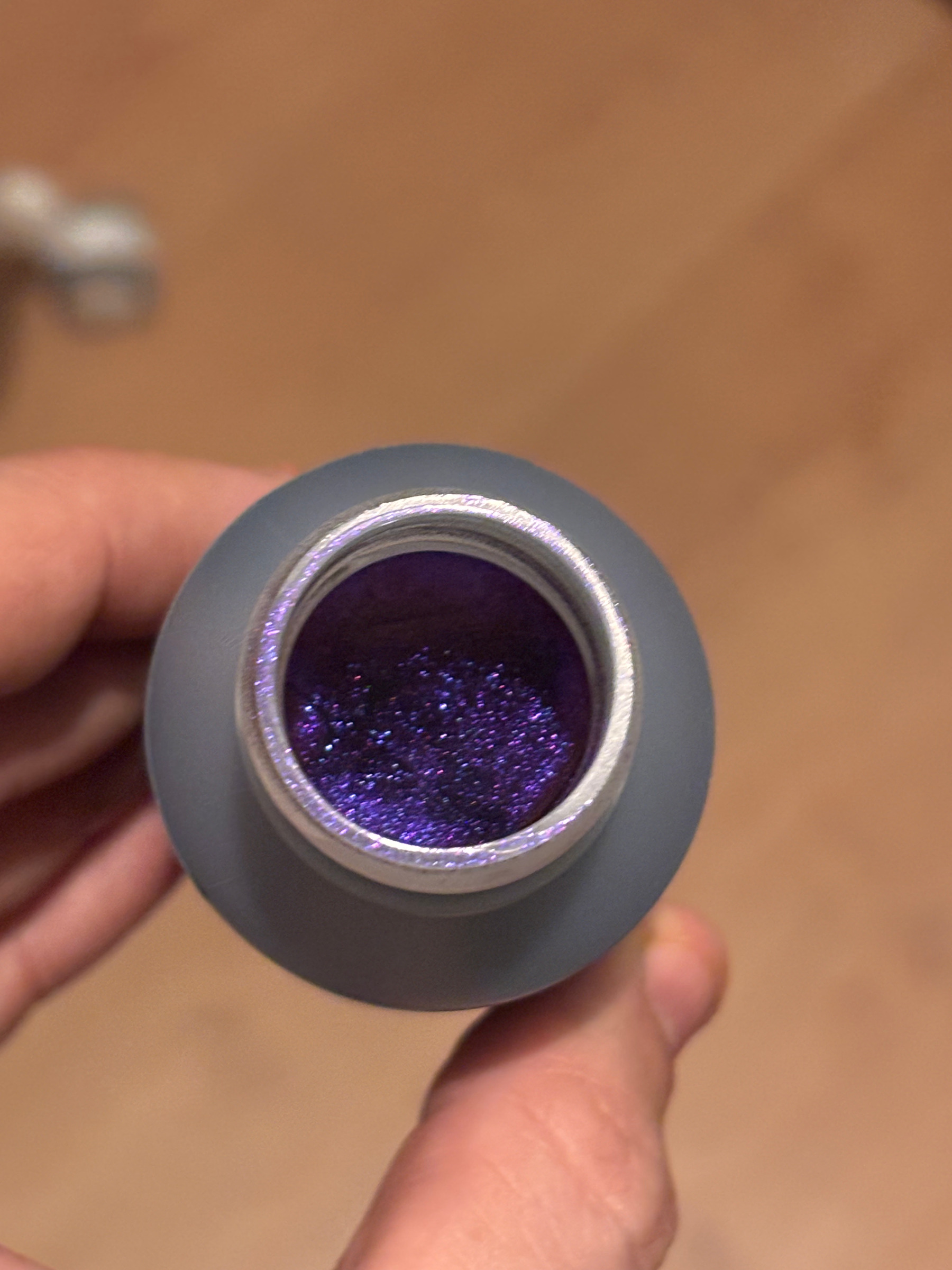 A small jar of metallic violet pigment, held in one hand