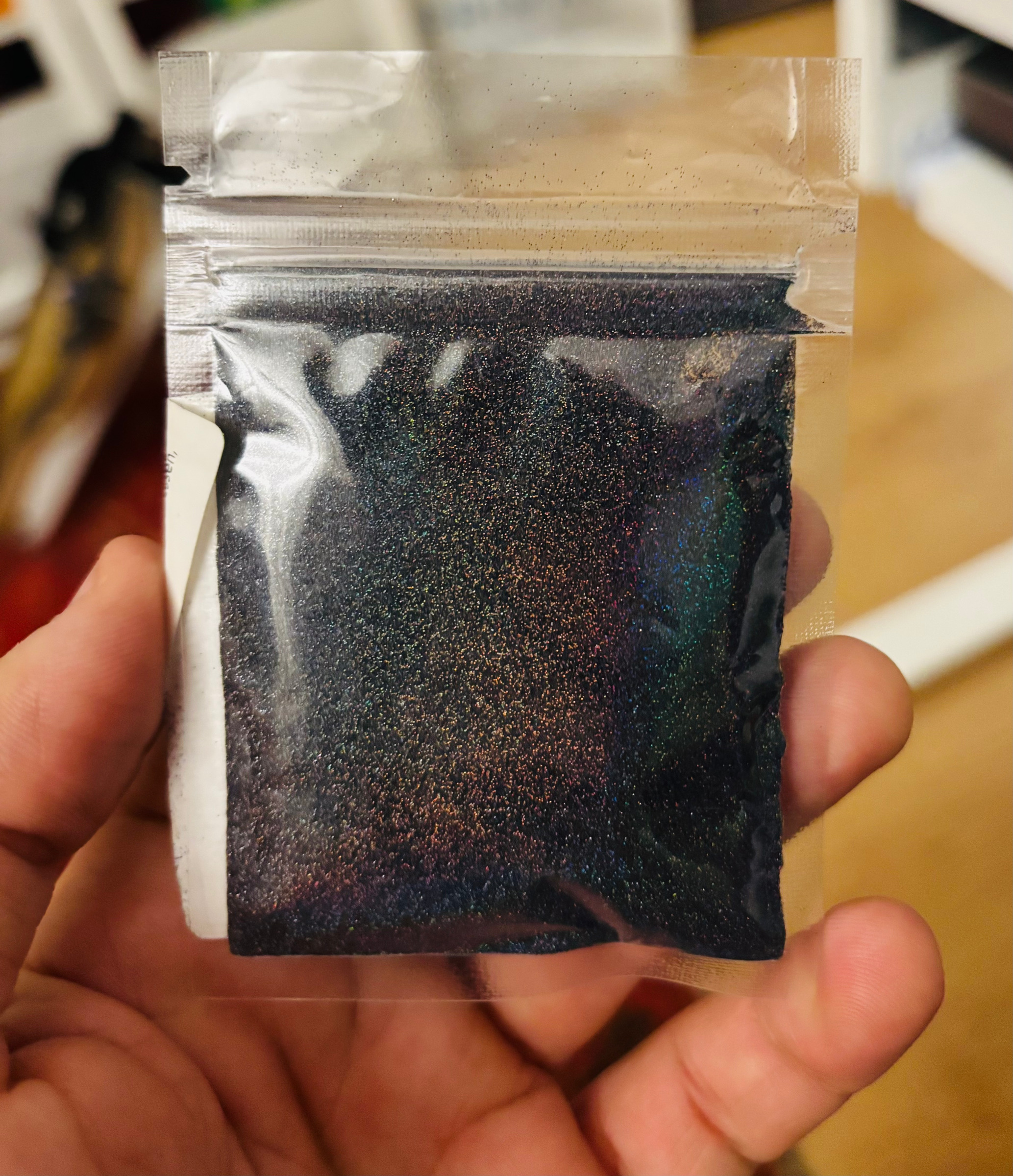 A small bag of dark pigment with iridescent glints, held in one hand
