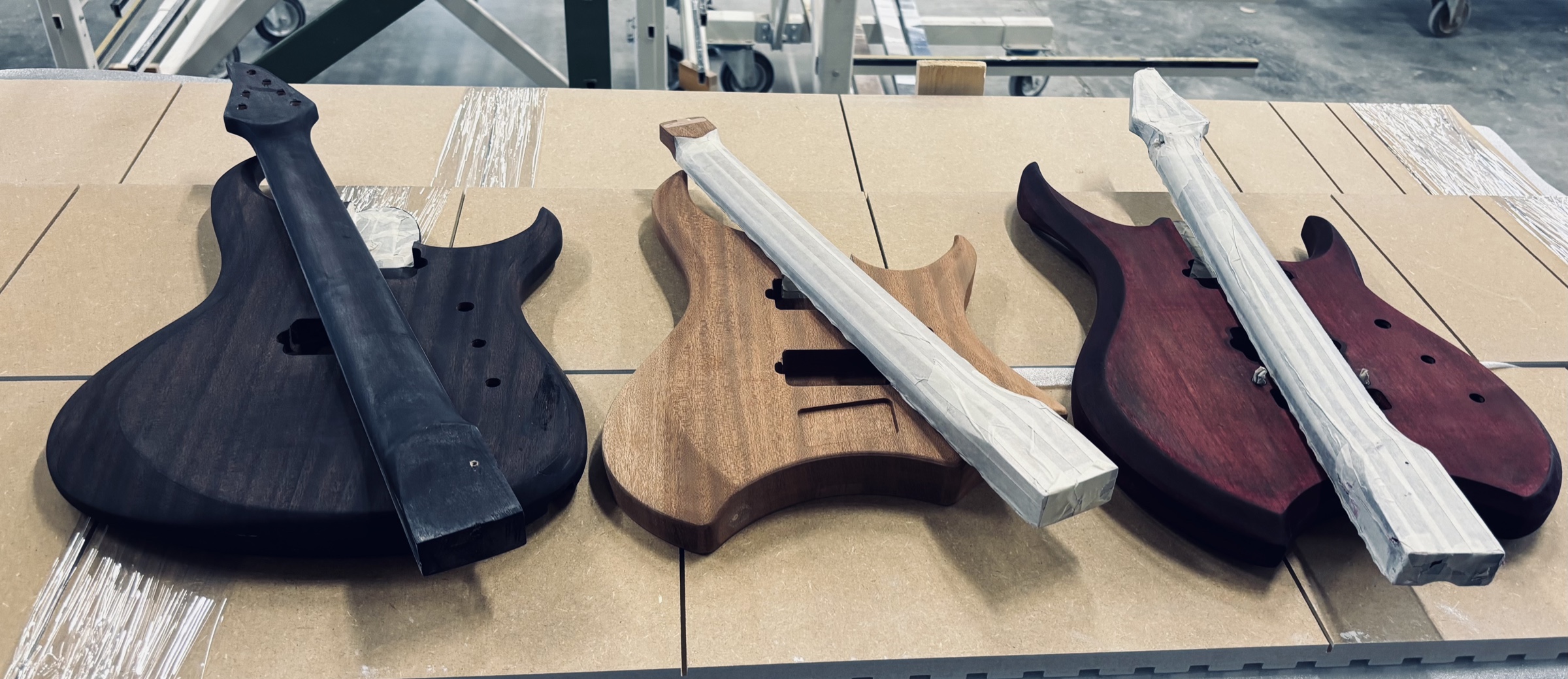 Three guitar bodies in different woods, resting on the bench