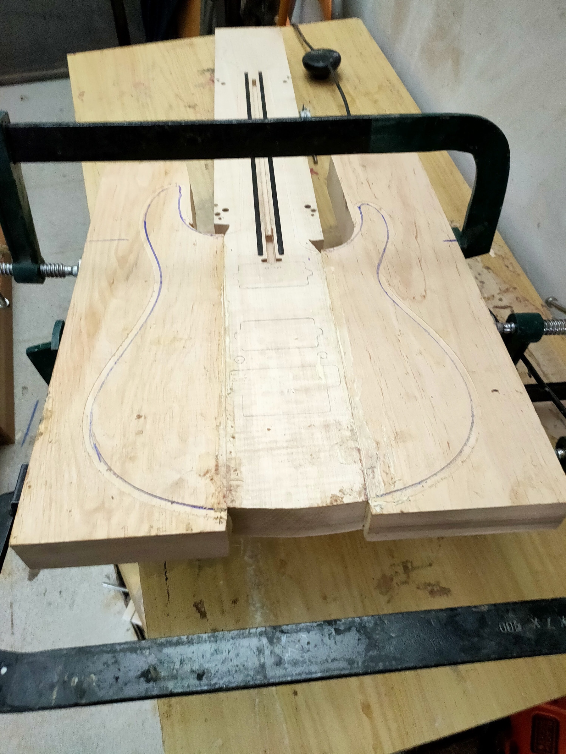 The outline of a body traced on the wood, the blank still held in clamps