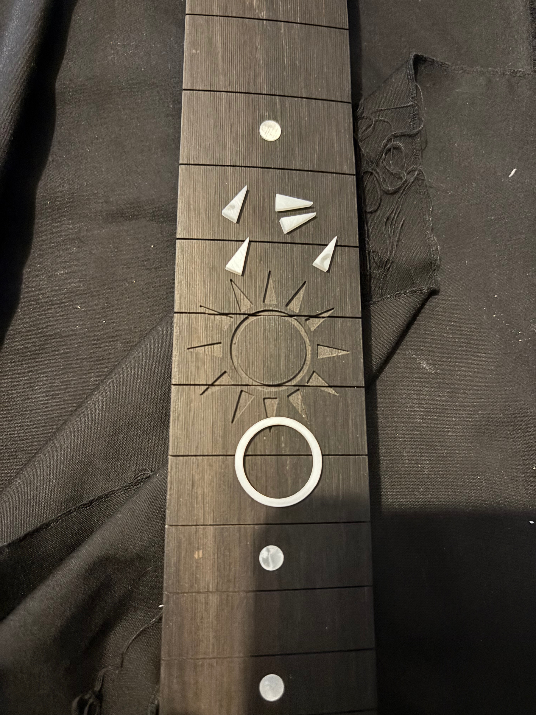A sun cut into an ebony fingerboard, with the mother-of-pearl rays already cut beside it