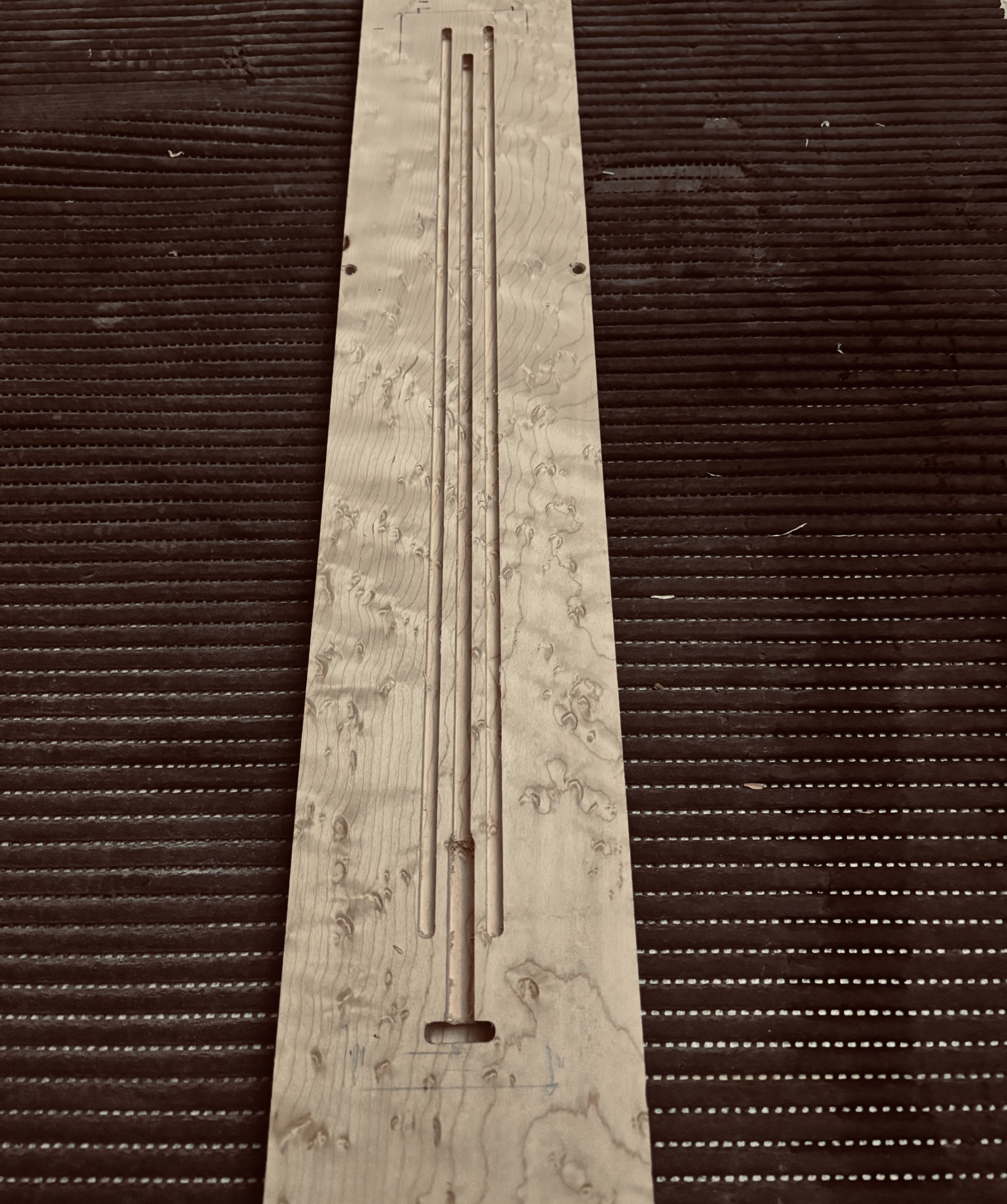 A bird's-eye maple neck with its three channels cut: one for the truss rod, two for the carbon rods