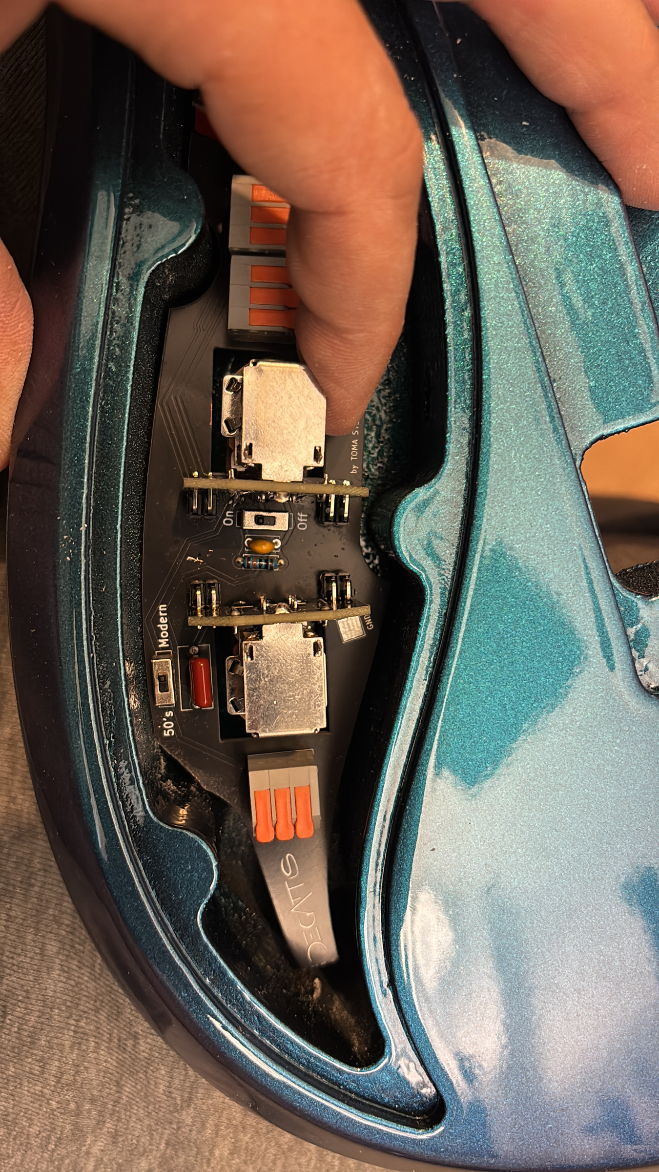 A hand setting the circuit board into the cavity of a teal body