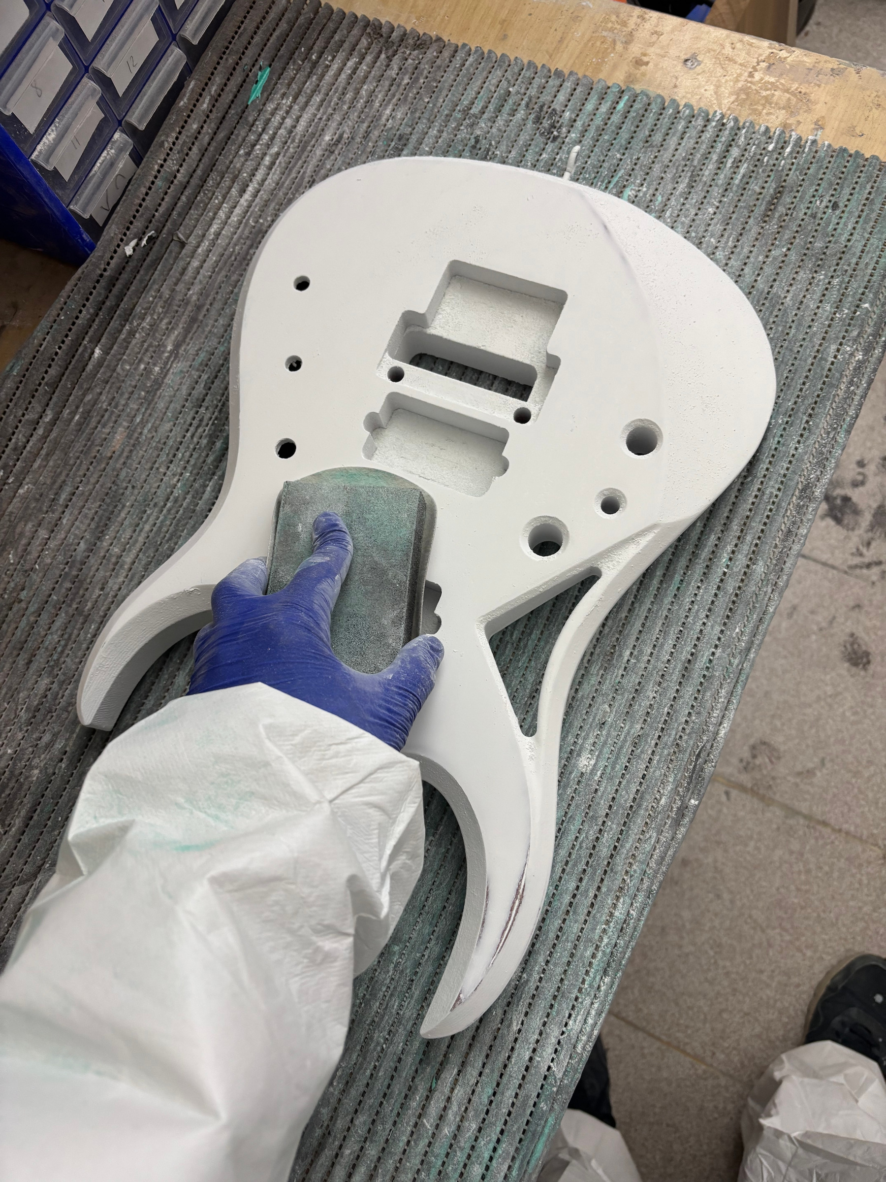 A gloved hand sanding a white body on the bench grid