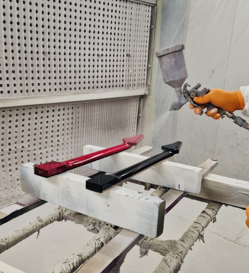 A gloved hand spray-finishing two necks, one red and one black, in the booth